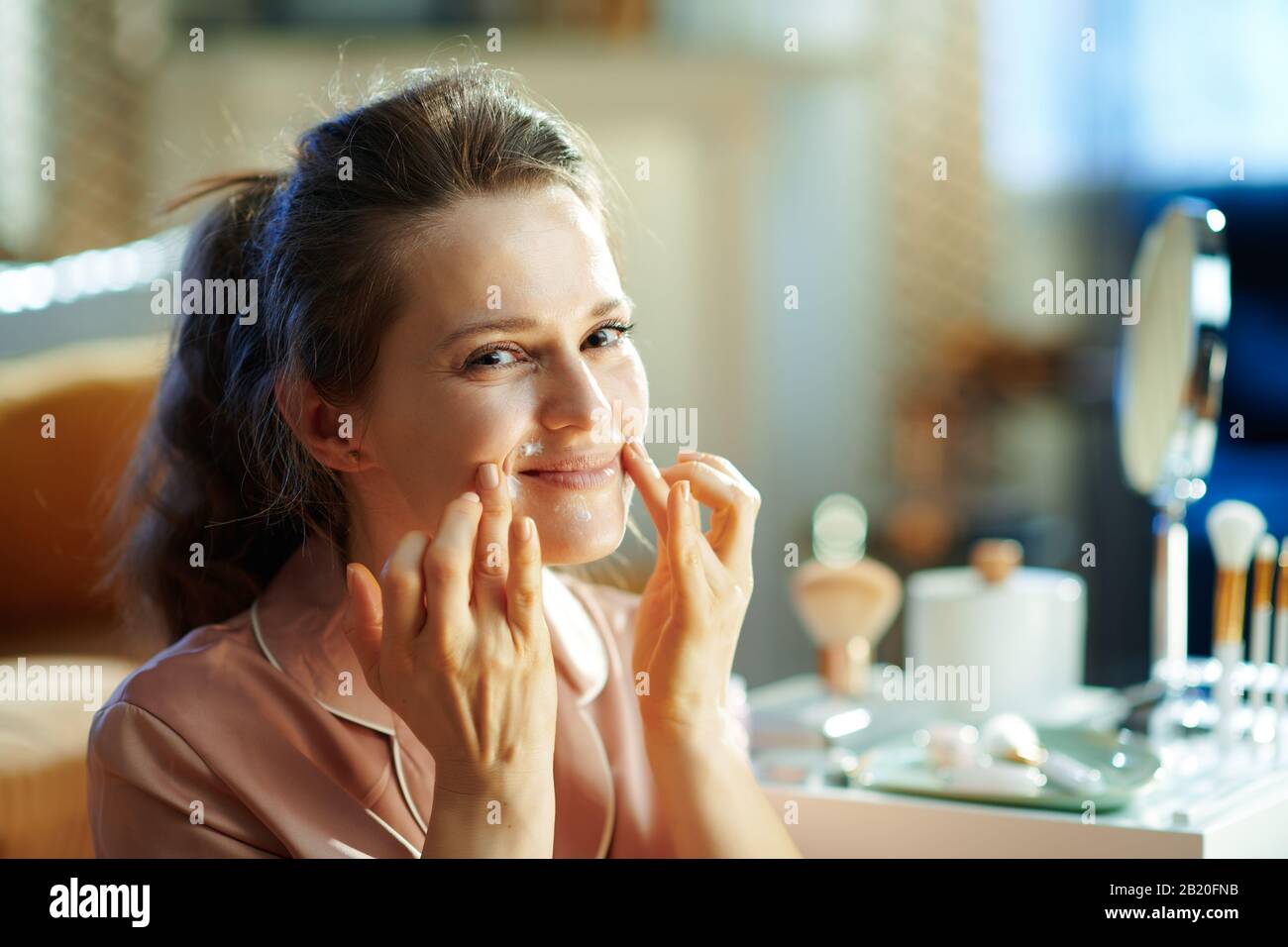 happy modern woman in pajamas at modern home in sunny winter day applying lip contour cream. Stock Photo