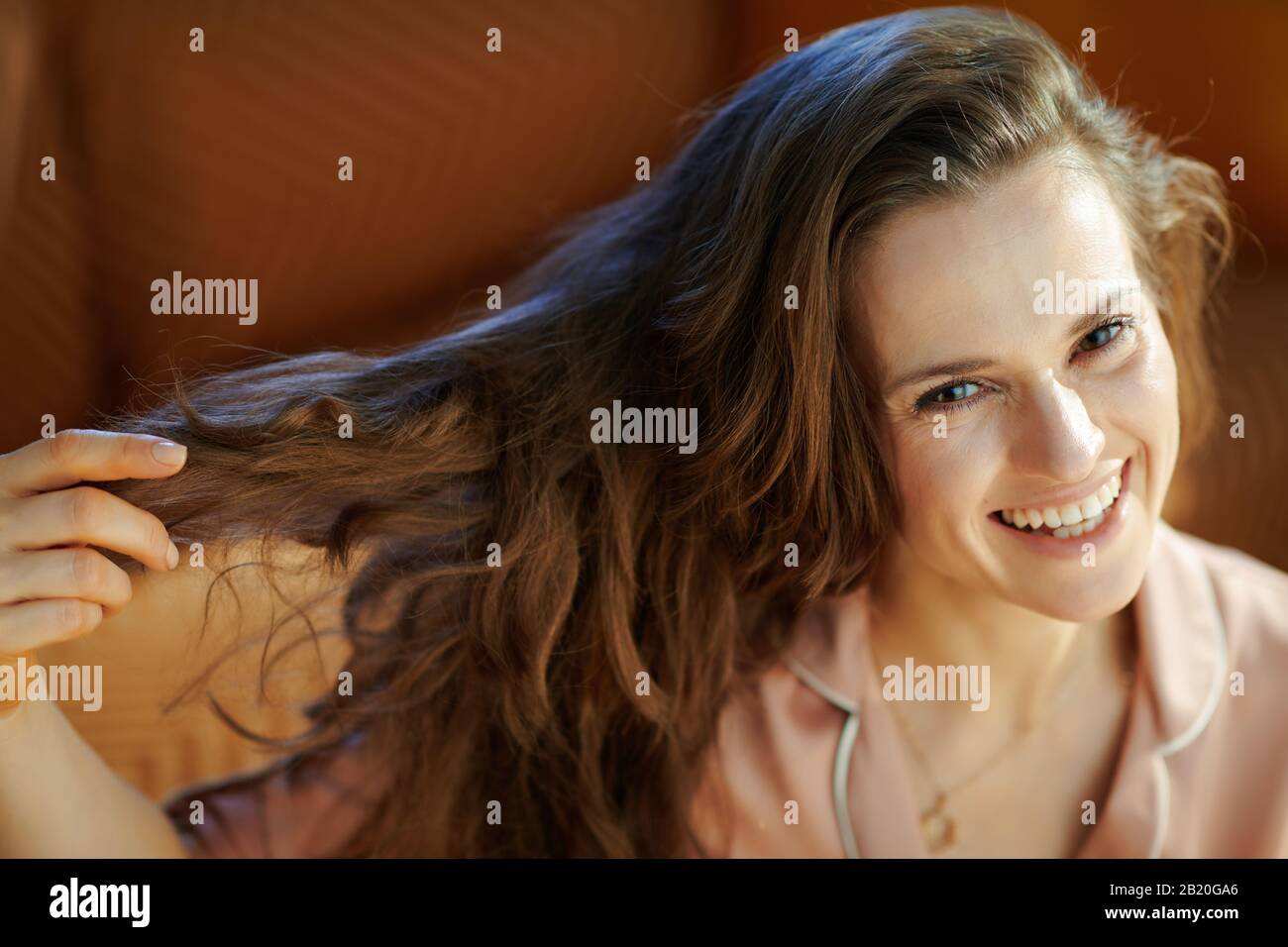 happy young housewife in pajamas with long brunette wavy hair in the modern living room in sunny winter day. Stock Photo