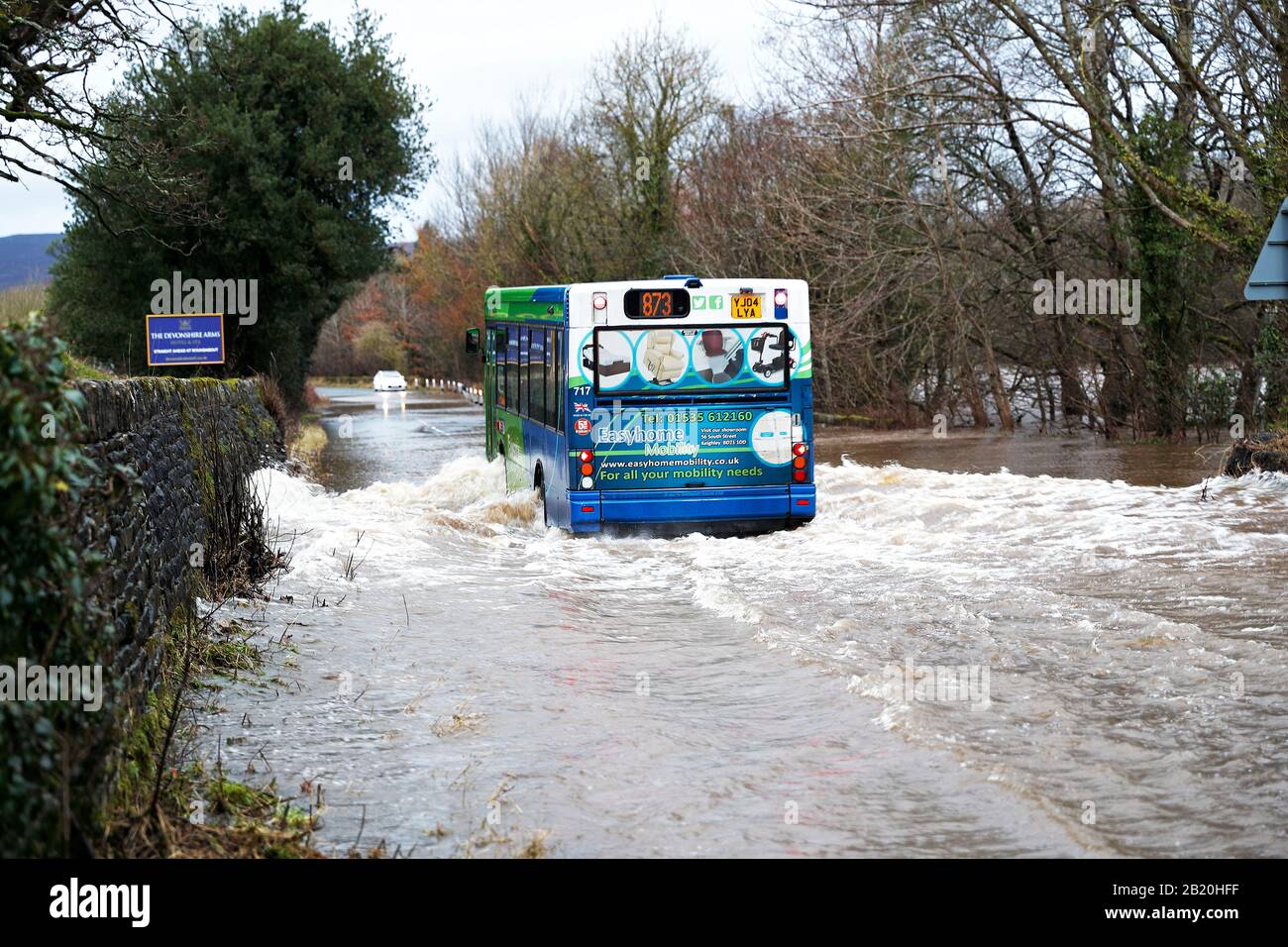 A bus travels along a flooded road where the River Wharfe has burst its banks in Addingham West Yorkshire during storm Dennis 09-02-20 Stock Photo