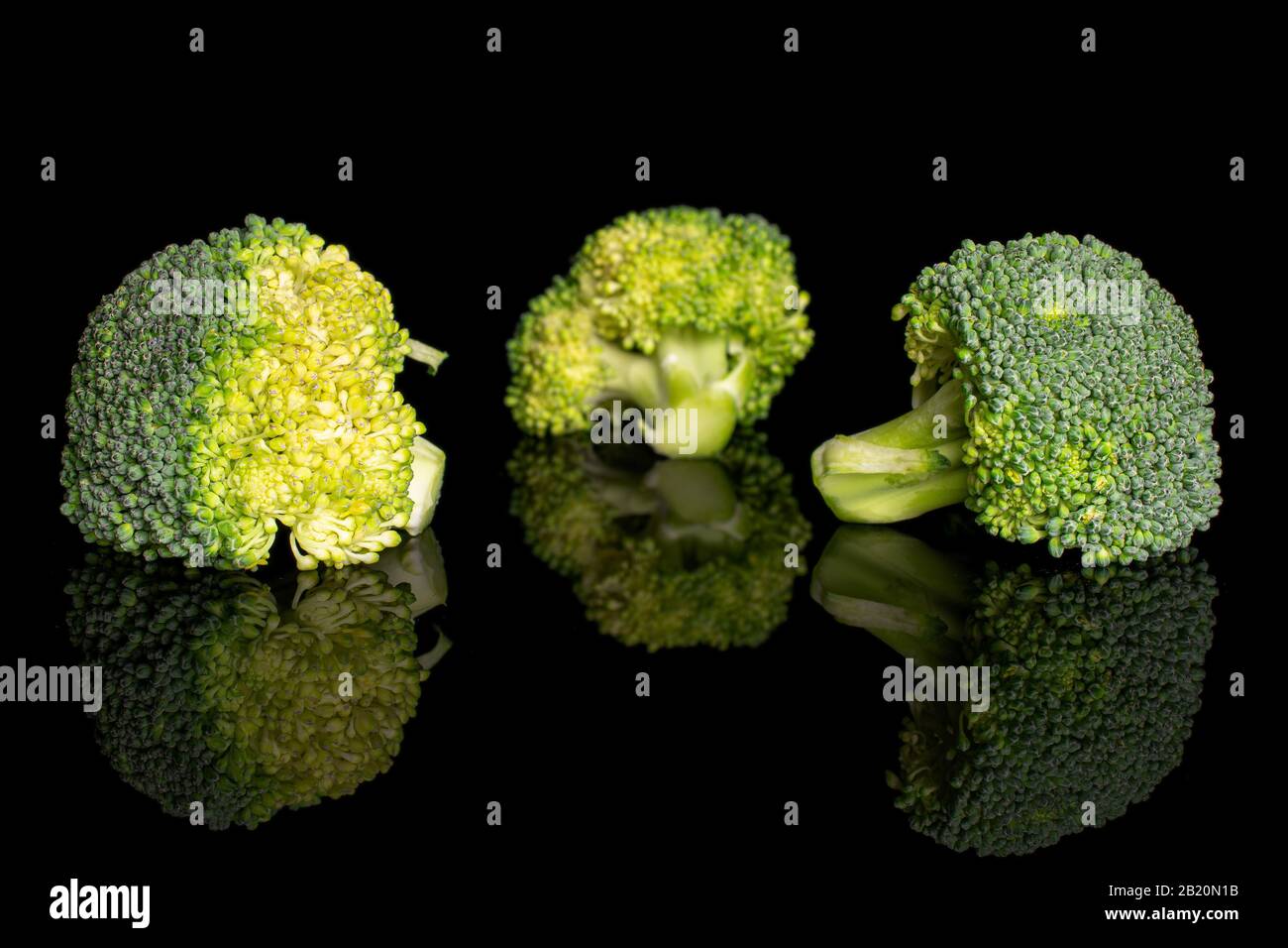 Group of three whole fresh green broccoli head isolated on black glass ...