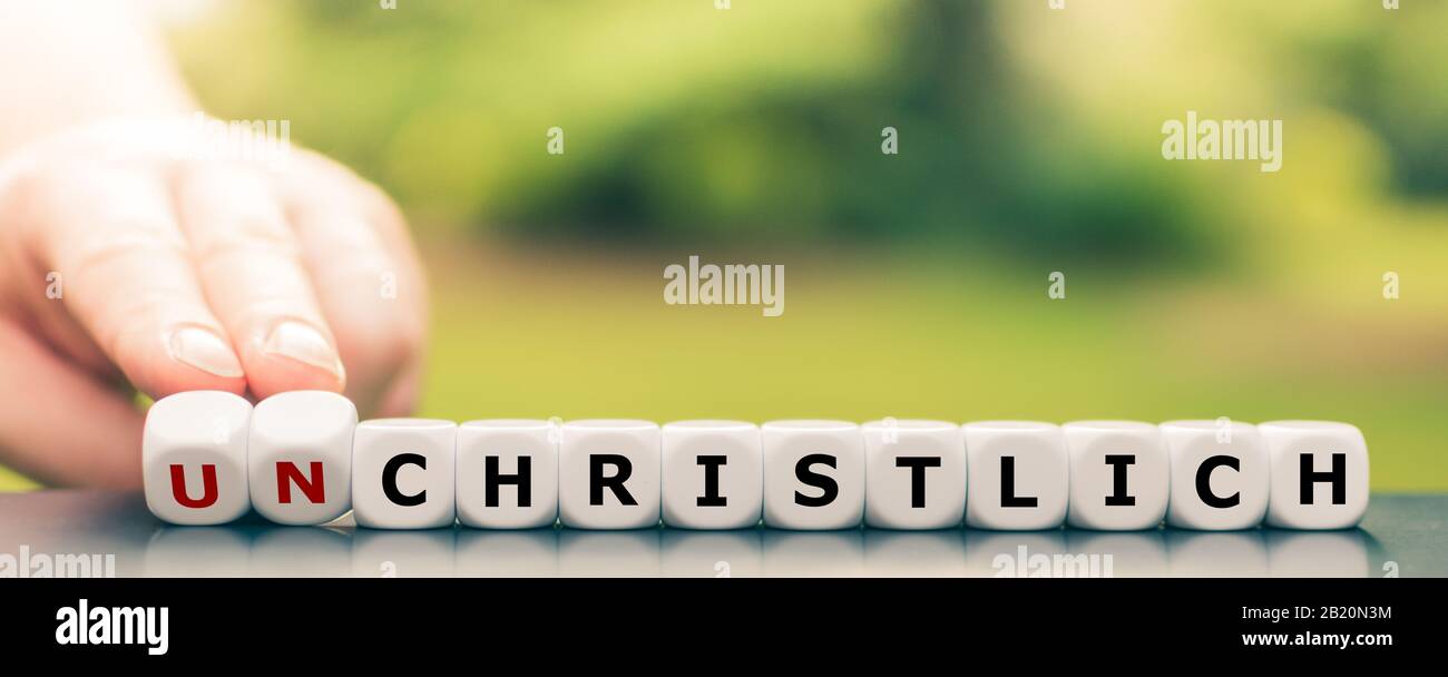 Hand turns dice and changes the German word 'unchristlich' ('unchristian') to 'christlich' ('christian'). Stock Photo