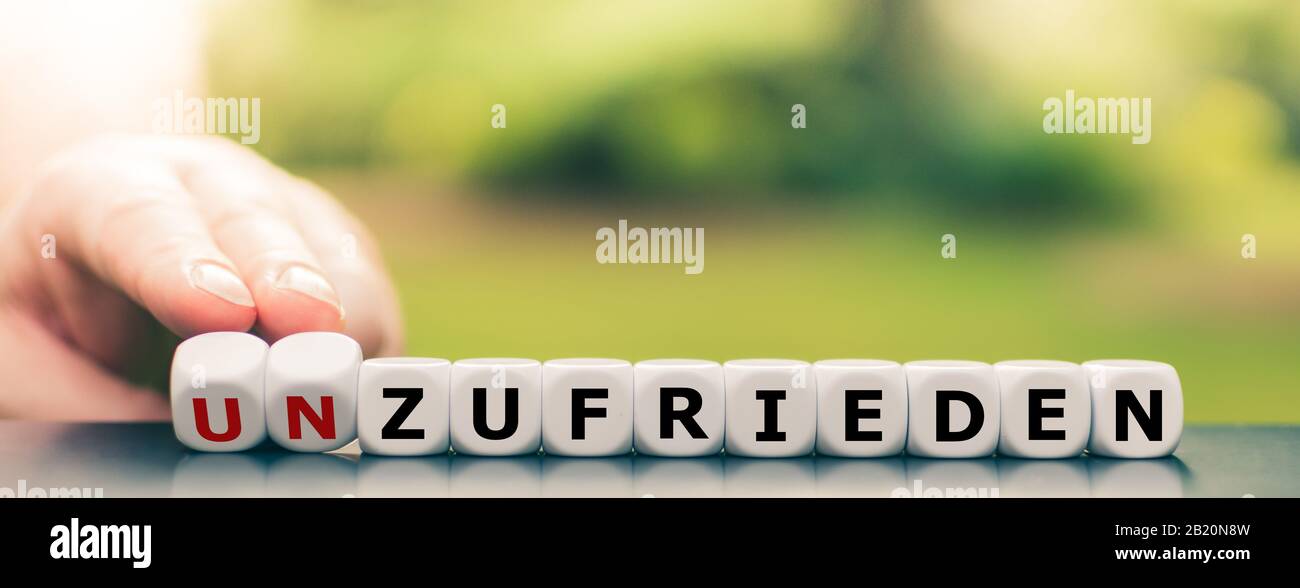 Hand turns dice and changes the German word 'unzufrieden' ('unhappy') to 'zufrieden' ('pleased'). Stock Photo