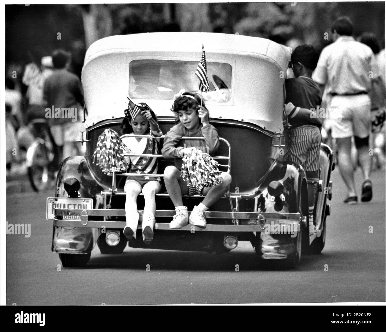 Two girls riding on the back of a 1930's car with flags having a good time after a parade in Kansas Stock Photo