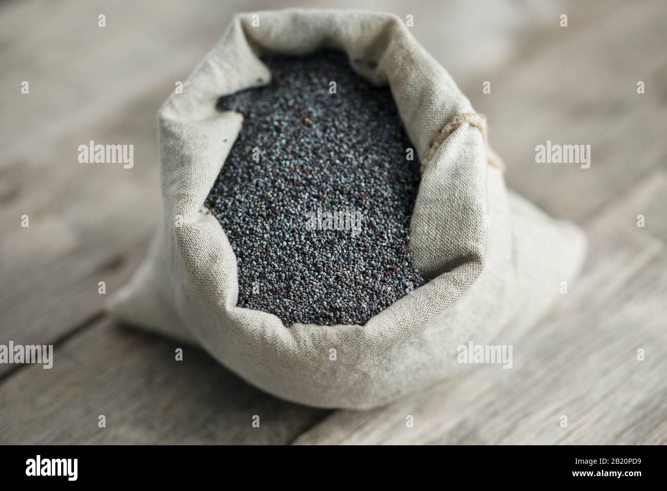 Poppy seeds in a burlap bag on a vintage wooden gray background. In