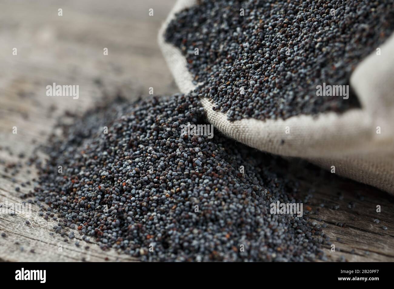 Poppy seeds in a burlap bag on a vintage wooden gray background. In