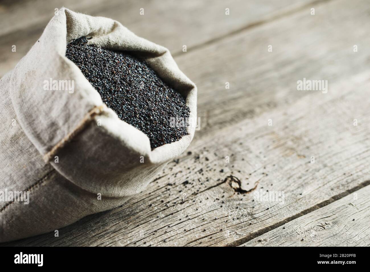 Poppy seeds in a burlap bag on a vintage wooden gray background. In