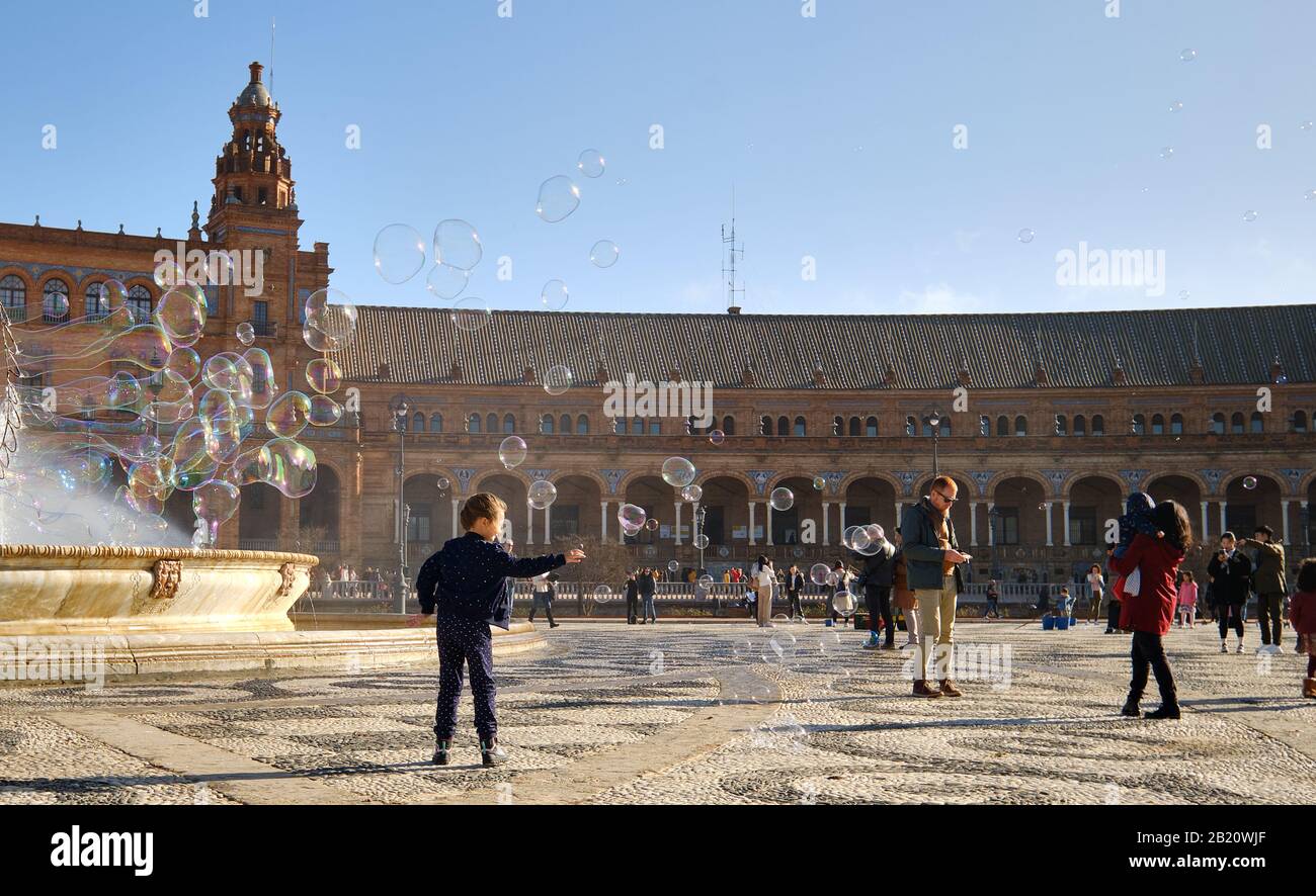 Sevilla, Spain - December 23, 2019: 6-7 year old girl running playing with flying soap bubbles having fun enjoy holidays on Plaza de España, Spain Stock Photo