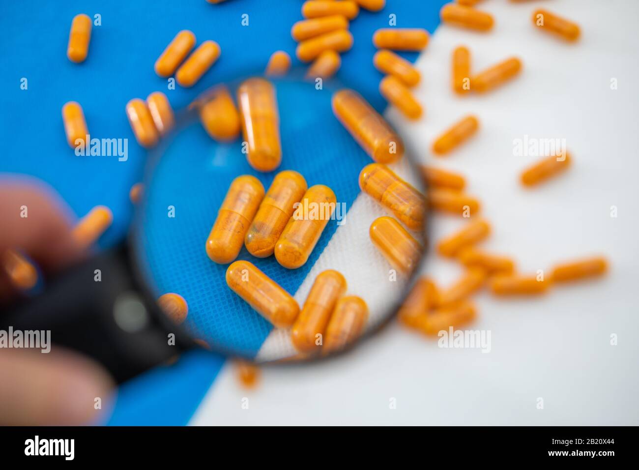 A magnifying glass shows the enlargement of some orange pills on a whiteblue background Stock