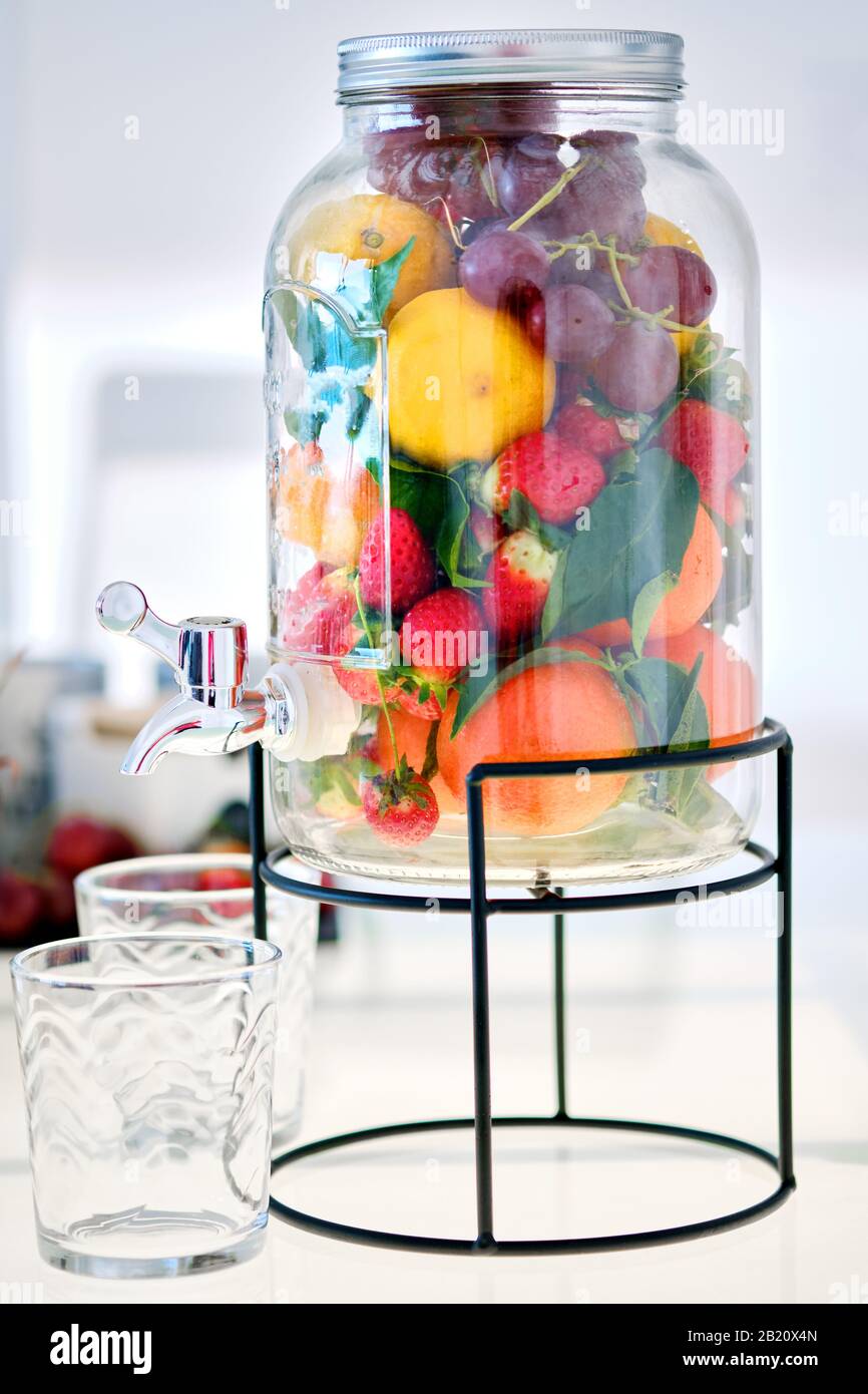 https://c8.alamy.com/comp/2B20X4N/close-up-view-glass-mason-gallon-jar-beverage-dispenser-with-stand-filled-with-fresh-ripe-multi-coloured-yummy-fruits-and-berries-and-empty-glasses-2B20X4N.jpg
