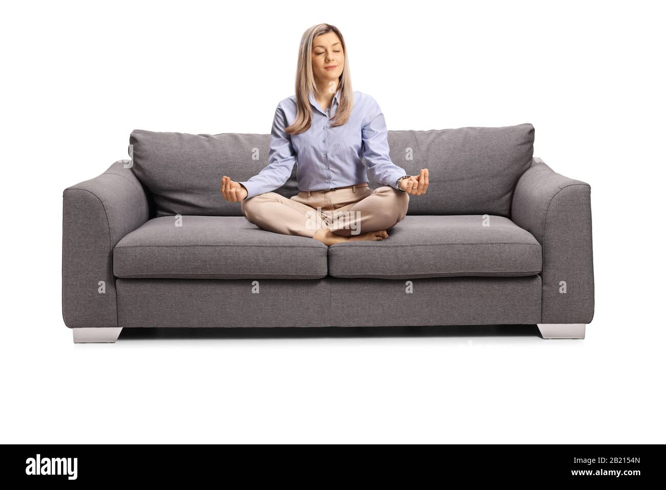 Young woman in formal clothes sitting on a sofa with crossed legs in a meditation pose isolated on white background Stock Photo