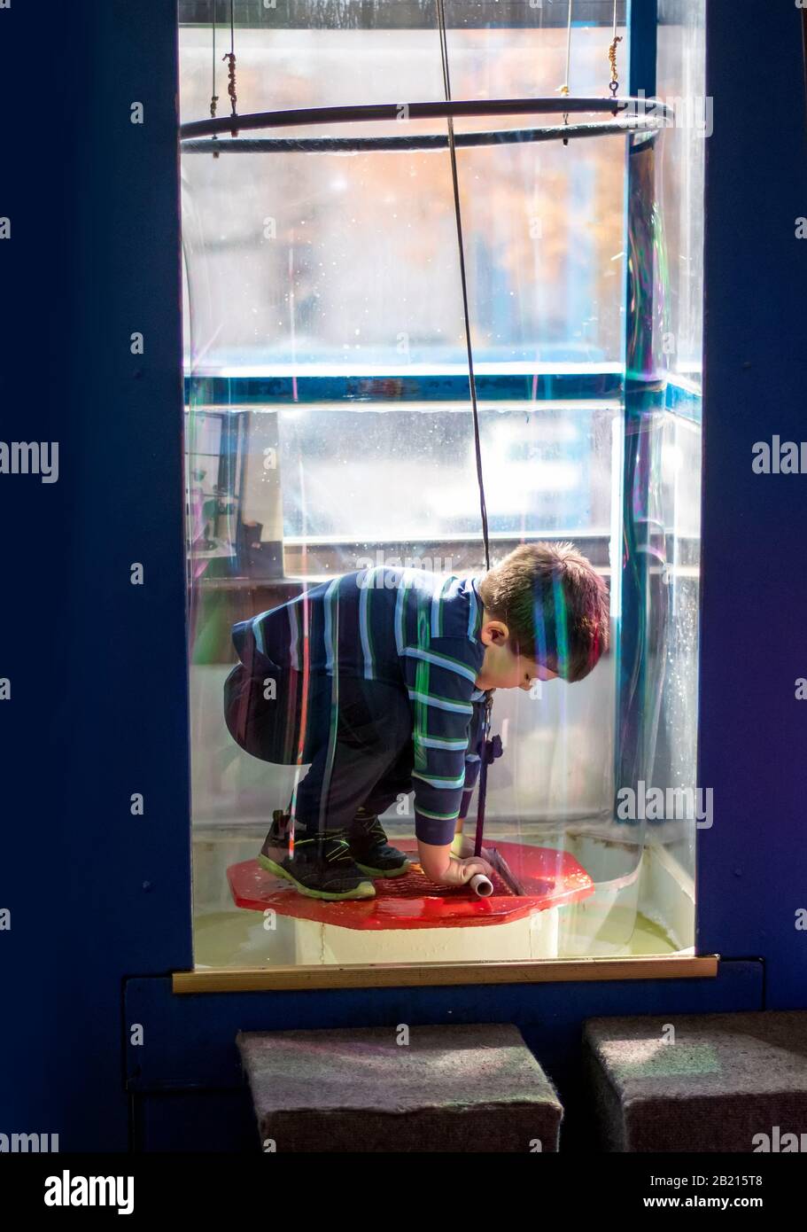 A young boy stands on a platform INSIDE a giant soap bubble, creating a science experiment at this Children s museum Stock Photo