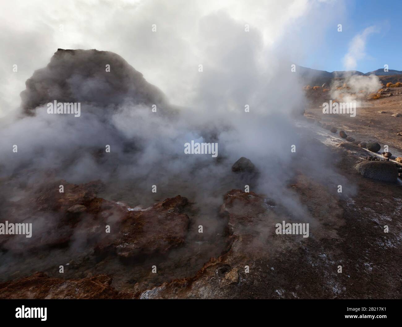 Steam rises from a geyser around a boulder at sunrise, El Tatio Geyser ...