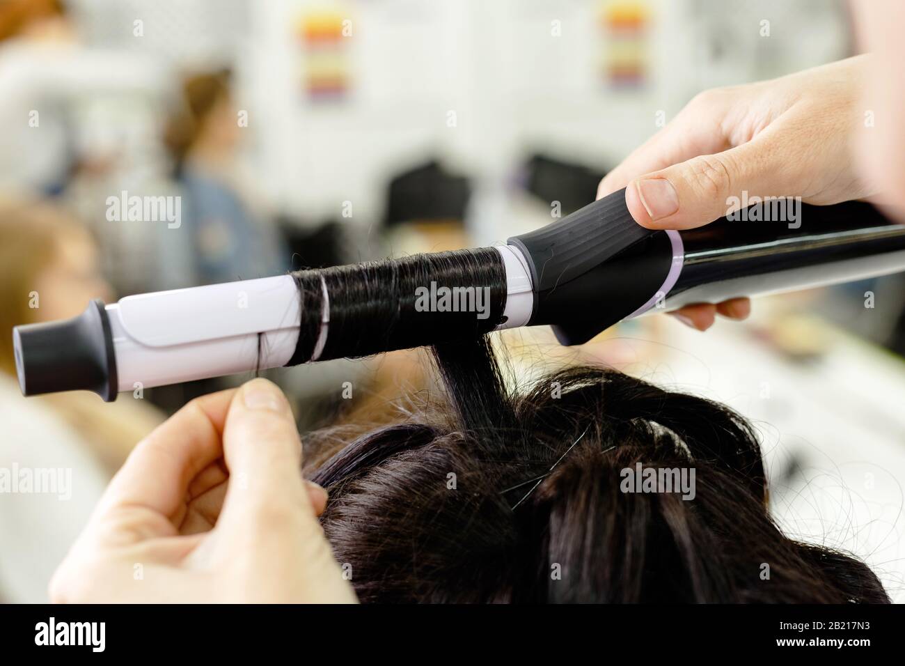 Hairstylist curling hair close up. Hairdresser making hairstyle to brown long hair woman in beauty salon. Professional hair care, Hairdressing Stock Photo