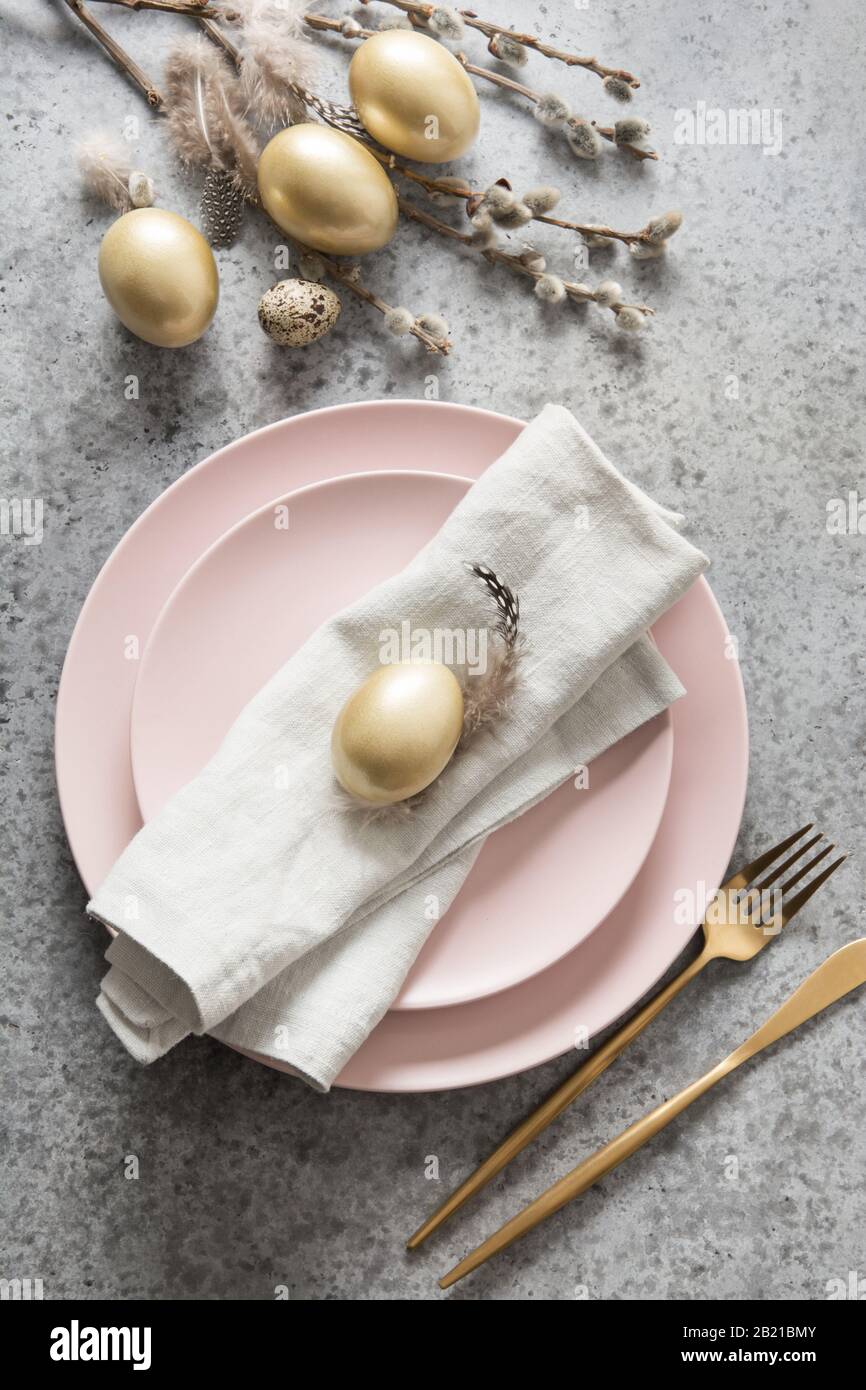 Easter table setting with pink plate and golden eggs on grey stone ...