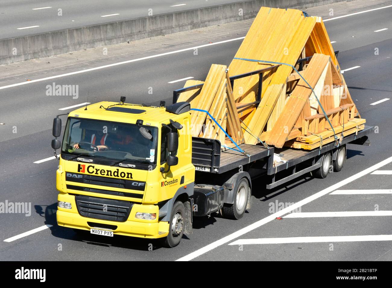 Prefabricated roof trusses by Crendon Timber Engineering business transported on company hgv lorry truck cab driver & low loader trailer UK motorway Stock Photo