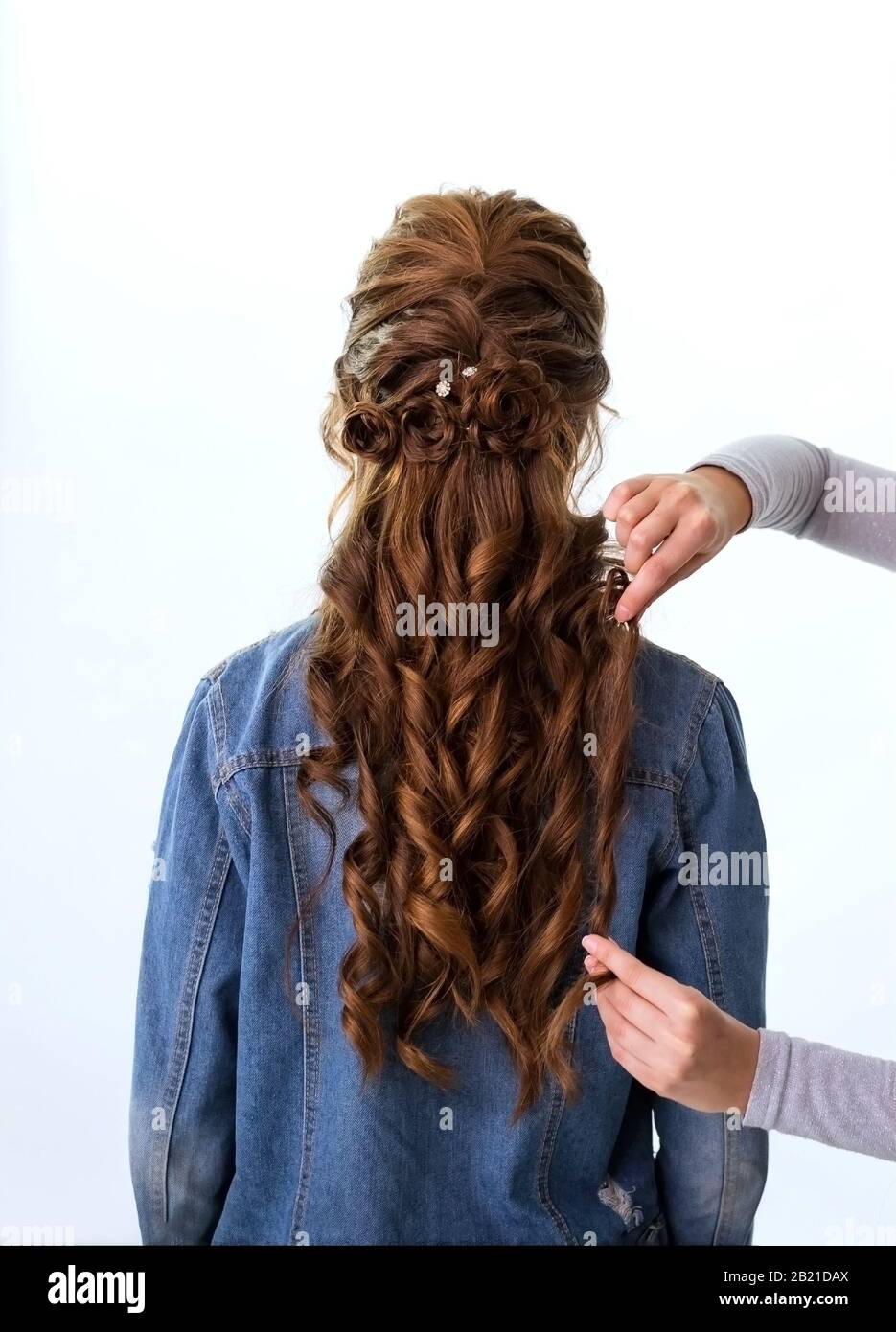Wave curls hairstyle. Hairdresser making hairstyle to red brown hair woman with long hair using comb on white background. Professional hairdressing Stock Photo