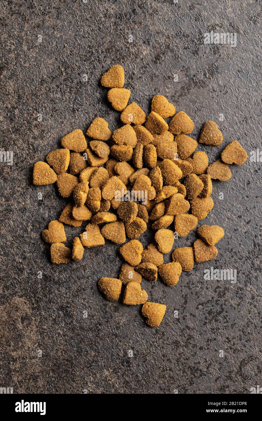 Dried kibble pet food. Heart shape dried animal food on old table. Top view. Stock Photo