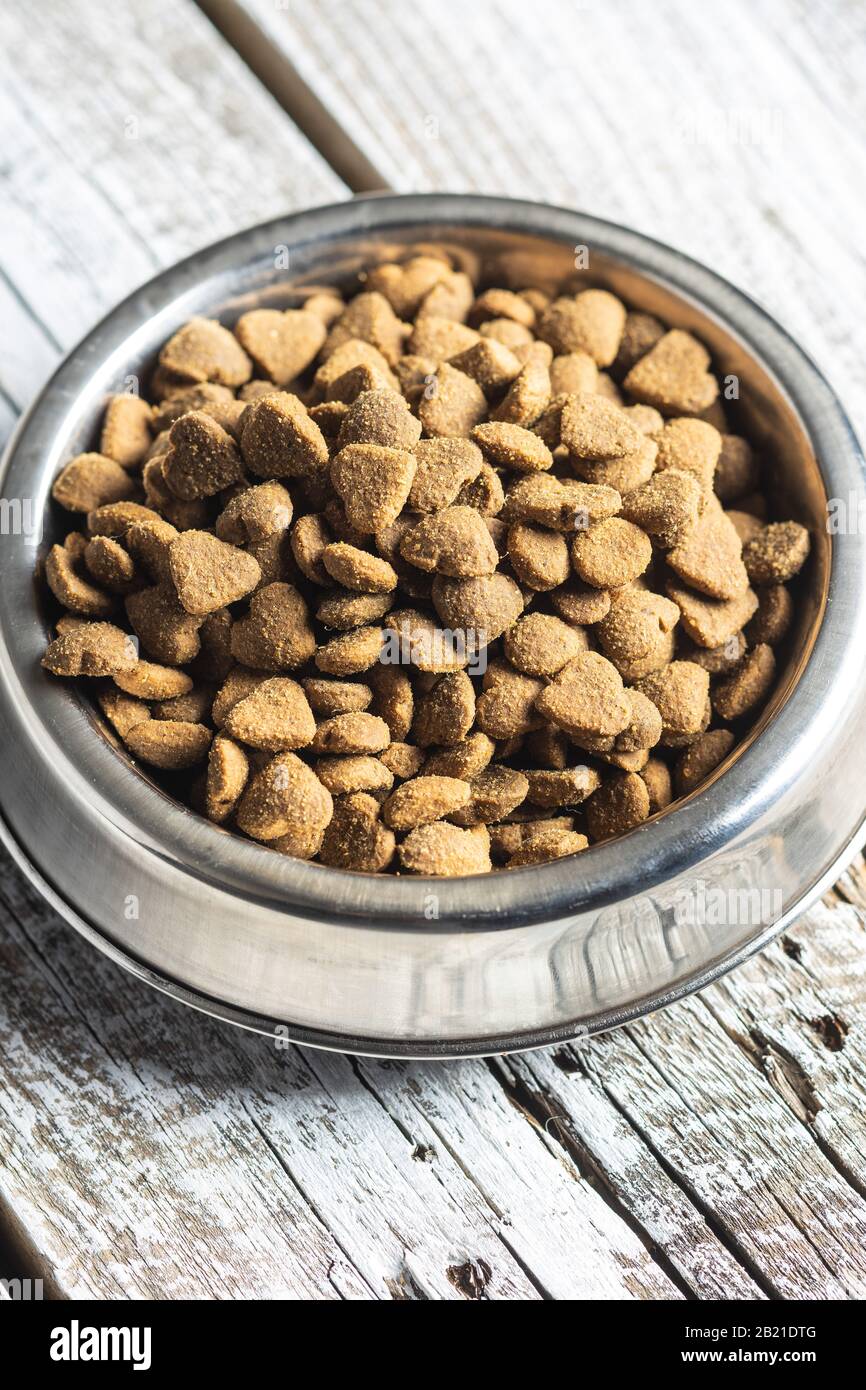 Dried kibble pet food in bowl. Heart shape dried animal food on old wooden table. Stock Photo