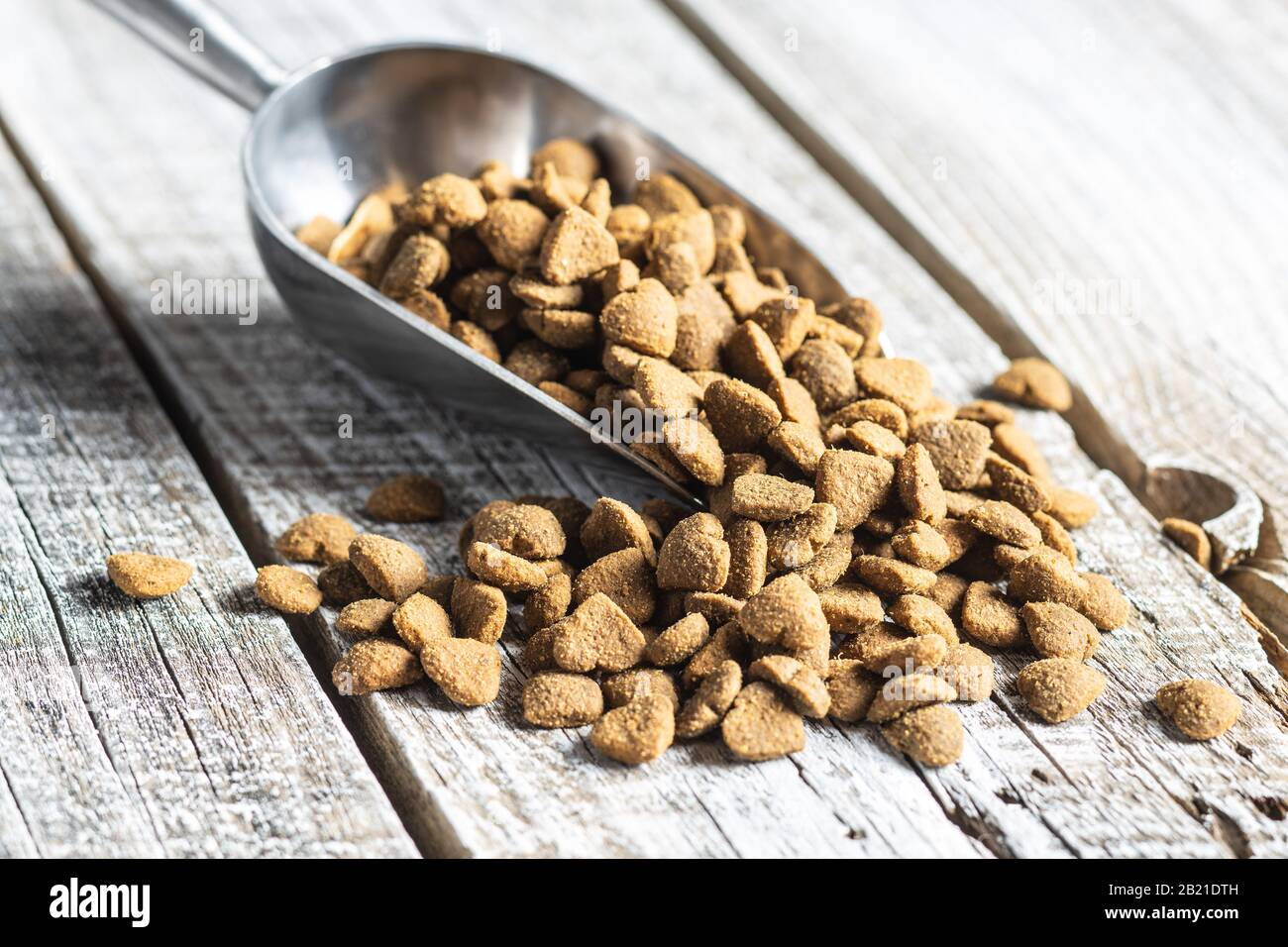 Dried kibble pet food in scoop. Heart shape dried animal food on old wooden table. Stock Photo