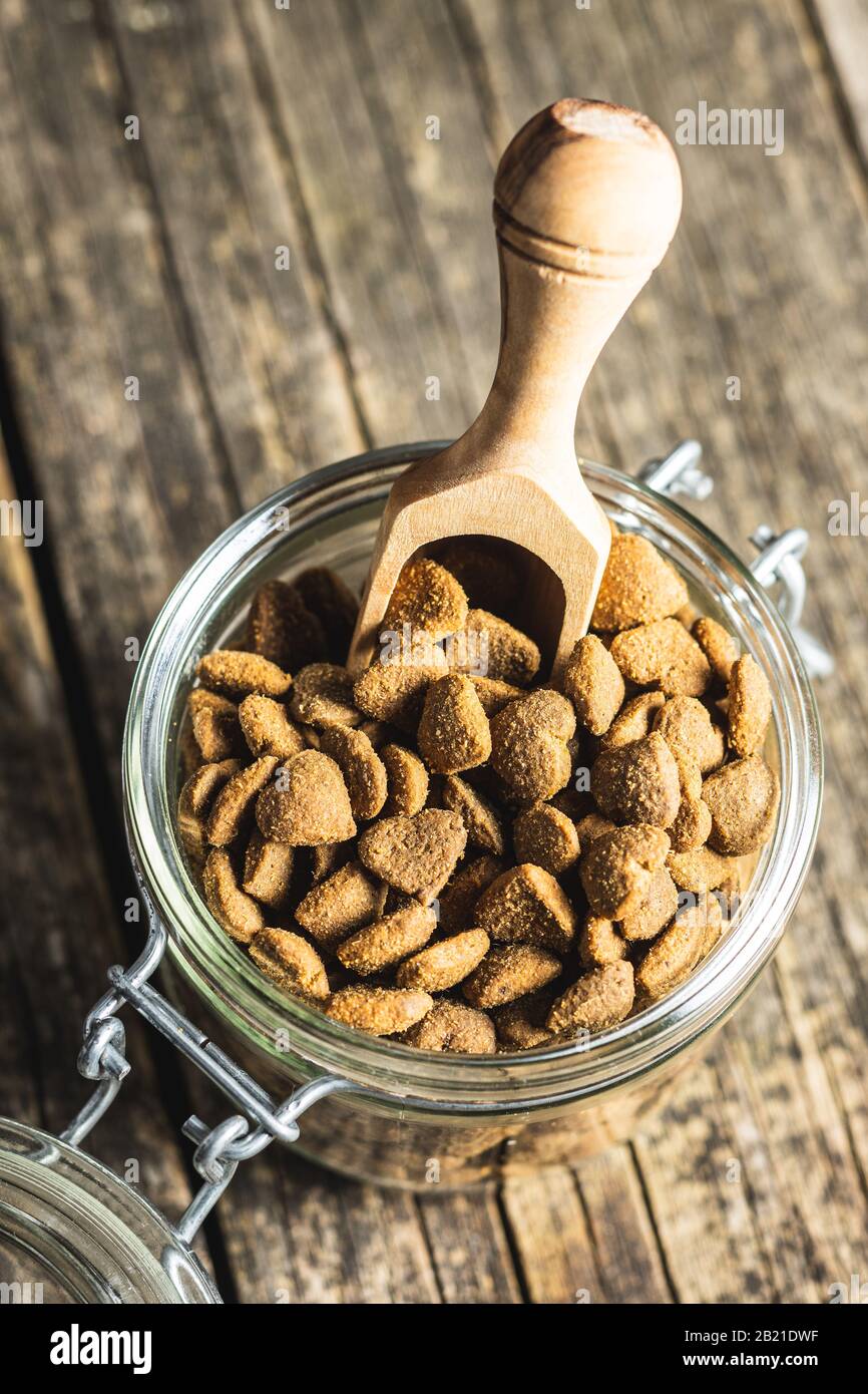 Dried kibble pet food in jar. Heart shape dried animal food on old wooden table. Stock Photo