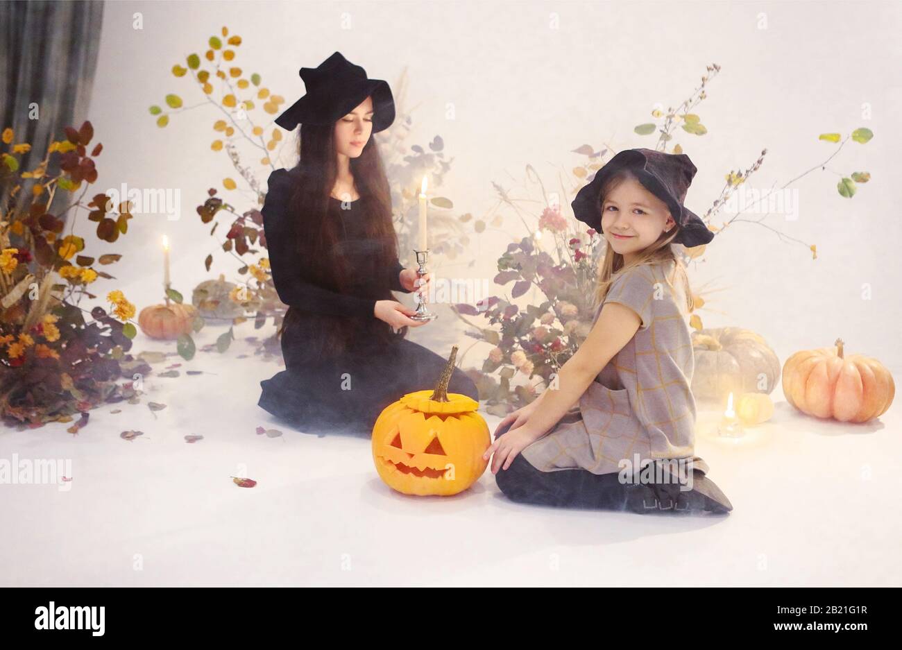 Happy mother and daughter wearing spooky black costumes of witches looking  at each other in studio with Halloween decorations Stock Photo - Alamy