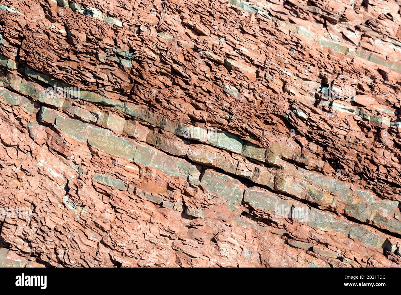 Layers of brown sedimentary rock in the side of a cliff. The rock is slanted at an angle. Closeup view. Stock Photo