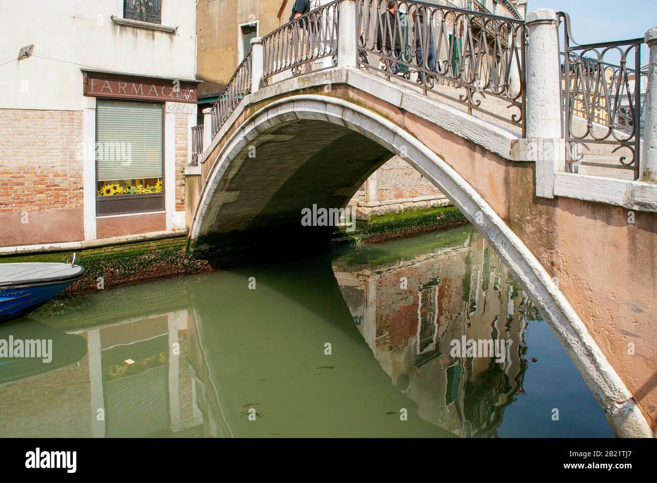 Reflection of a building in the green water of a small canal shows under one of the typical bridges. Stock Photo