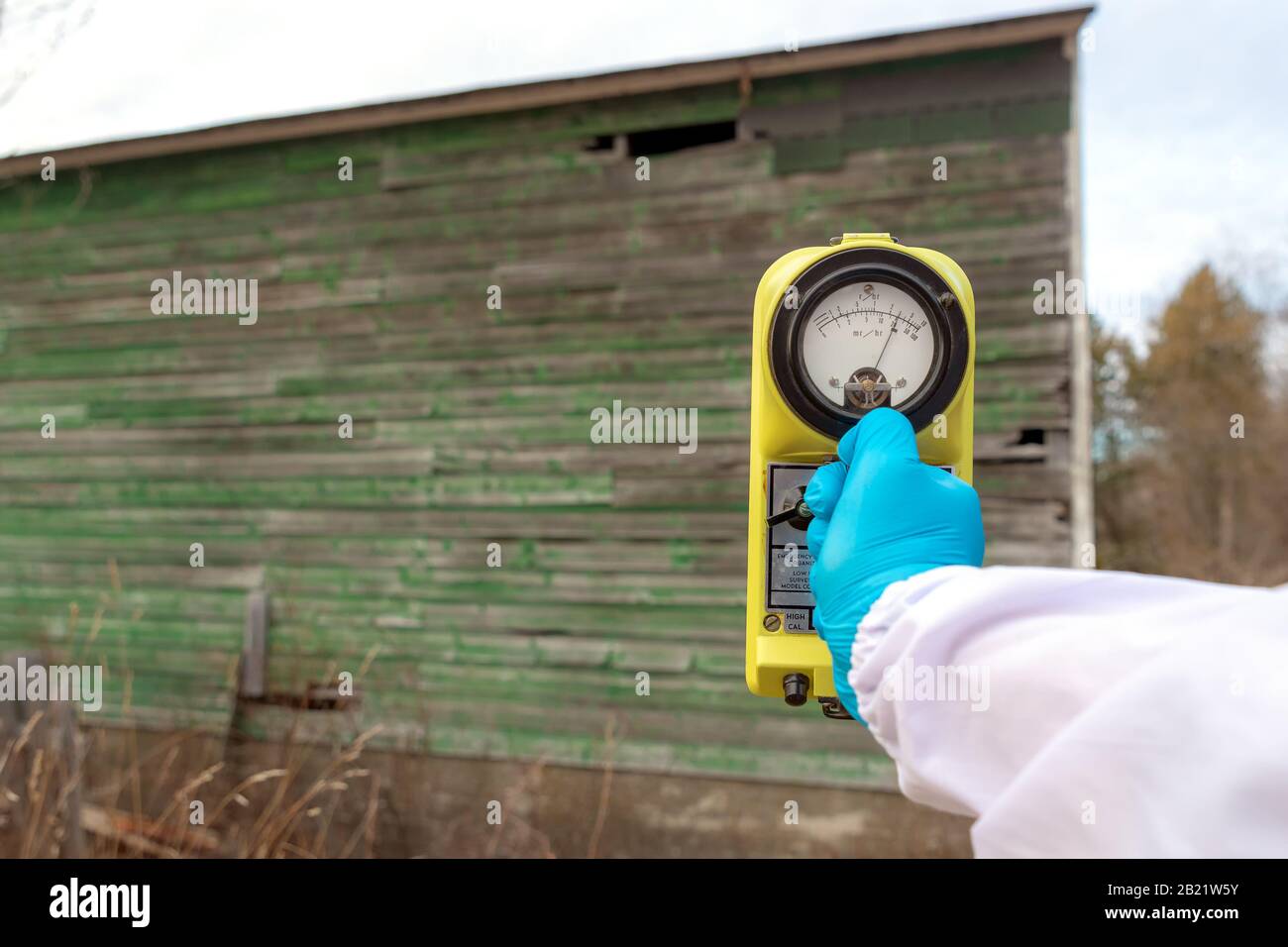 Measuring radiation at an old building. Blue gloved hand holds a radiation meter up to an old building, the needle shows a large amount of radiation. Stock Photo
