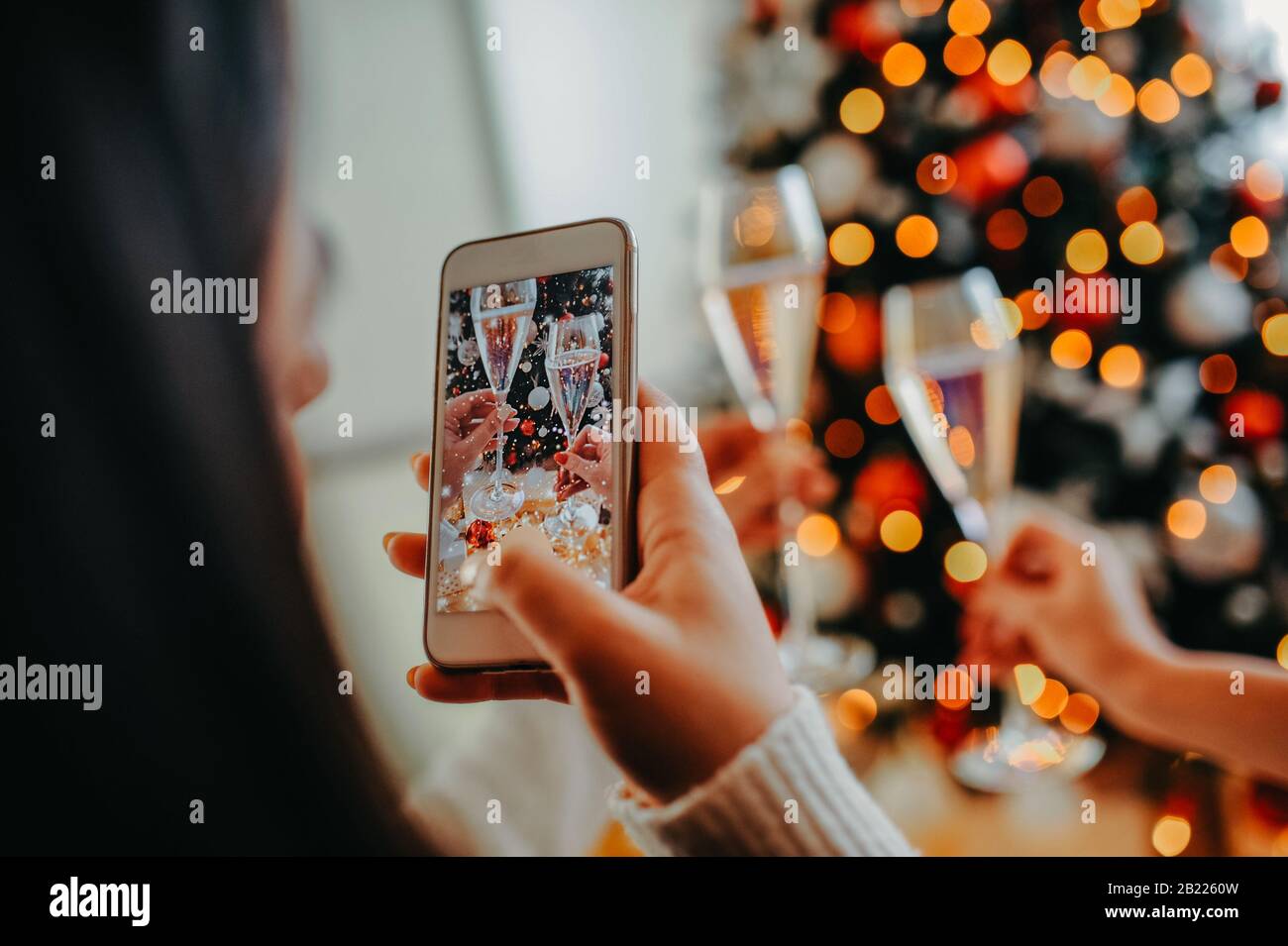 girl makes a photo on a white phone, two knocking glasses with champagne against the background of the Christmas tree in female hands Stock Photo