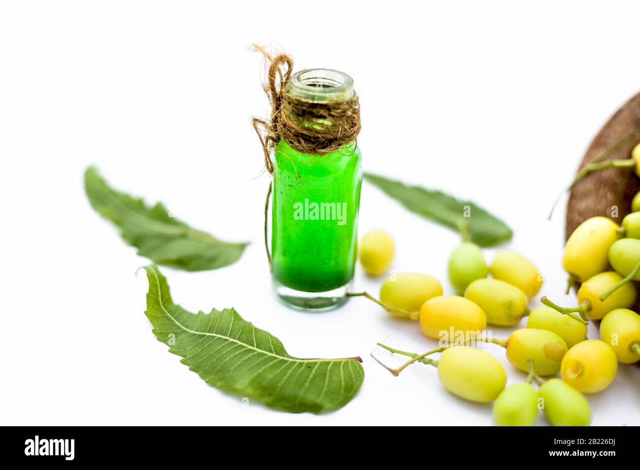 Fresh green neem fruit of Indian Lilac fruit in a clay bowl isolated on white along with its concentrated essential oil or essence in a transparent gl Stock Photo