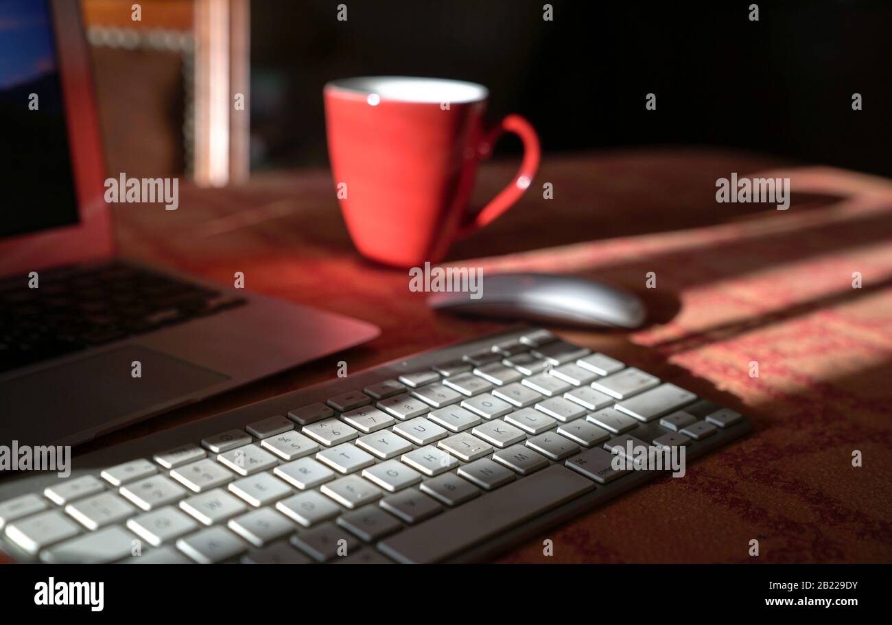 Laptop with wireless keyboard and mouse and coffee in red cup. Work from home or technology concept. Stock Photo