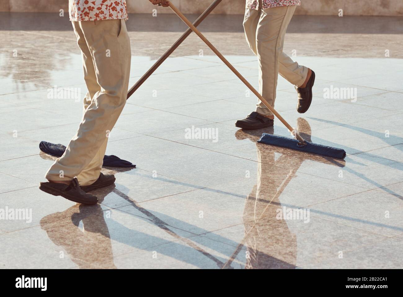 Two cleaners with mops cleaning marble floor outdoors. Cleaning service