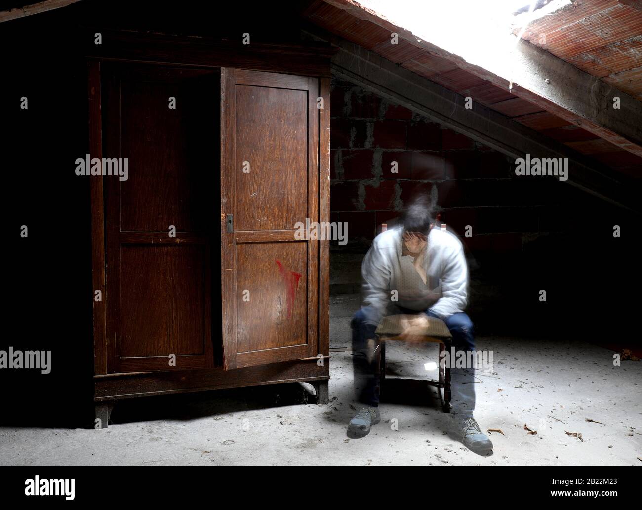 desperate spectral man on the chair in the attic with wooden wardrobe Stock Photo