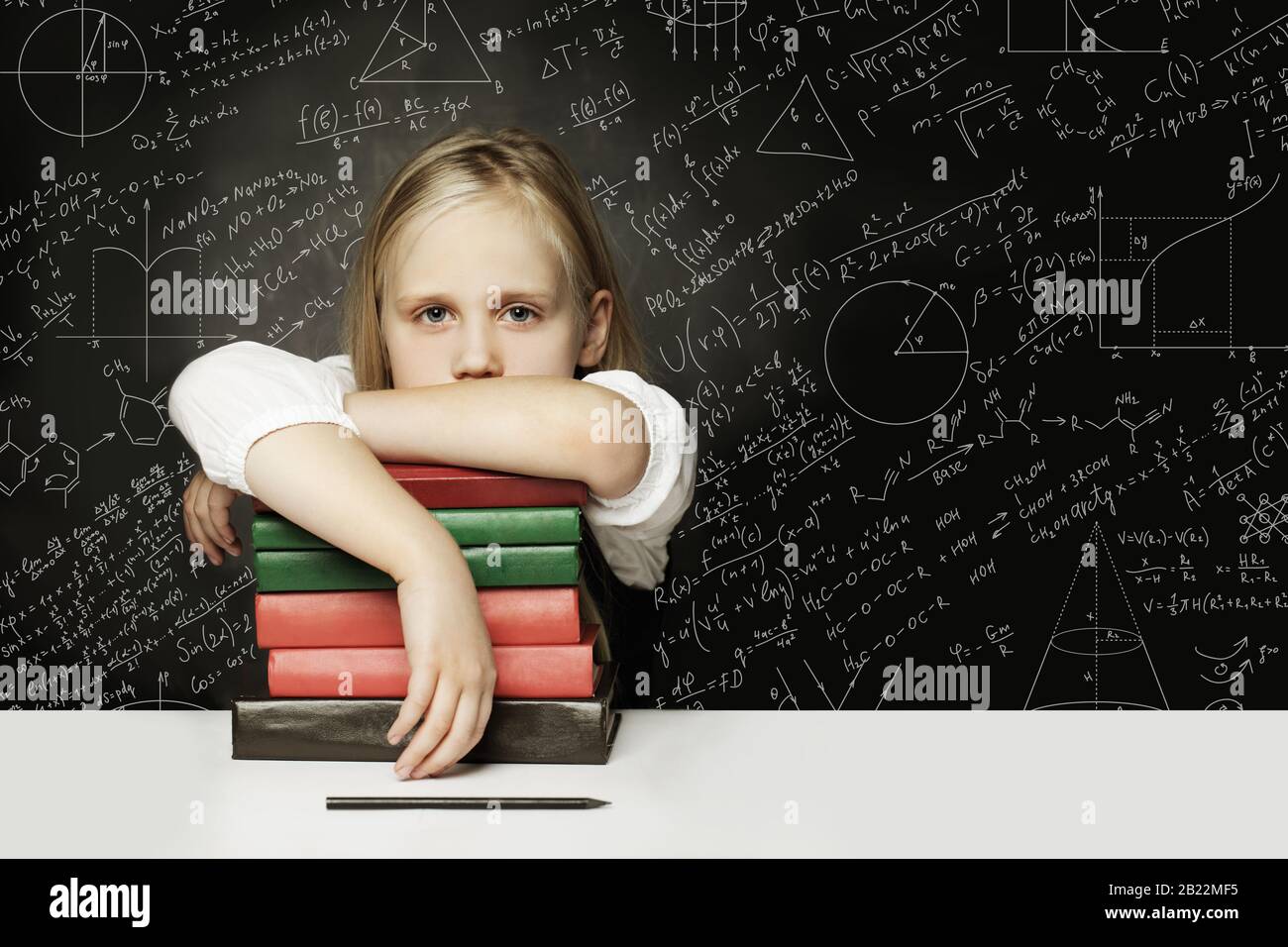 Tired child with books thinking on chalkboard with formulas Stock Photo