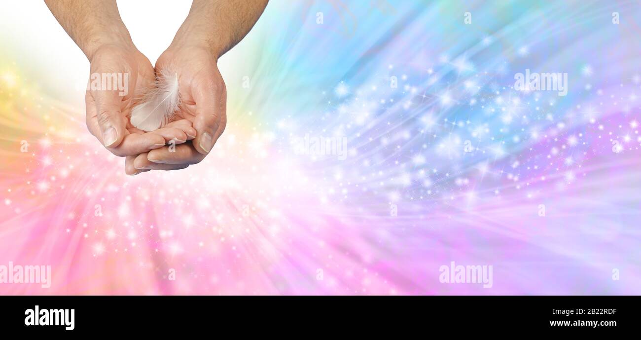Gentle Angelic Healing Hands Message Banner - male cupped hands offering a white feather against rainbow coloured sparkling flowing energy background Stock Photo