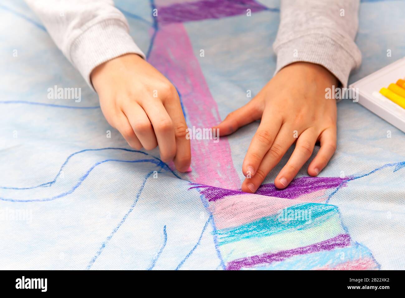 Simple kids hands drawing with precision on a huge canvas using oil pastels, coloring detail, closeup. Diy, children and art, creativity and creating, Stock Photo
