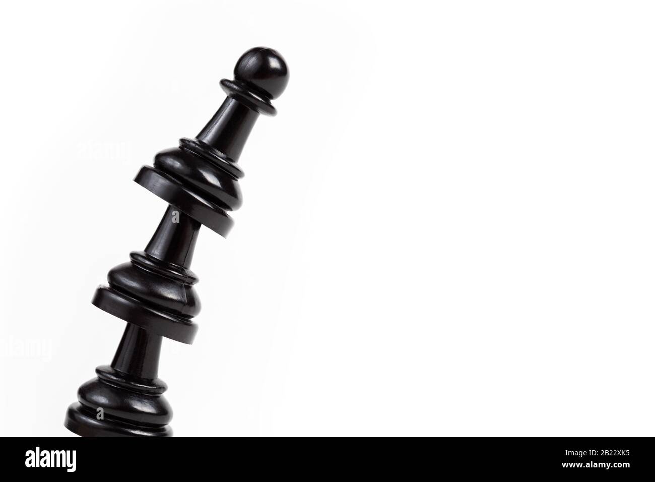 Simple leaning tower made of chess pawn pieces, curved bent construct of black game pieces placed on top of each other. Unstable shaky construction ab Stock Photo