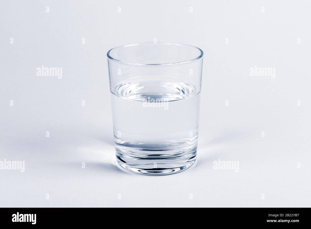 One simple half full half empty glass of fresh crystal clear clean drinking water, solo object isolated on light blue background. Hydration and health Stock Photo