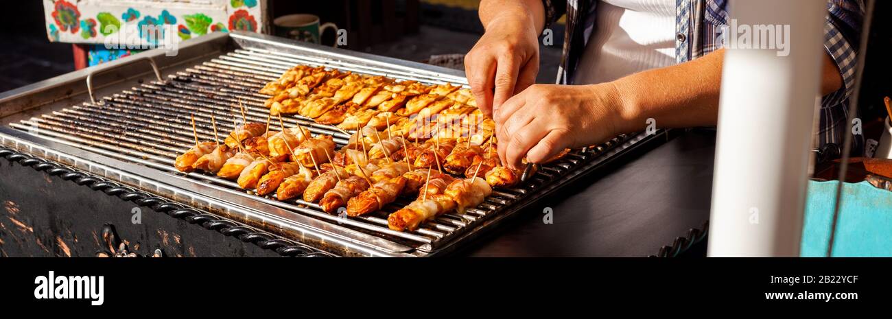 Woman preparing lots of traditional variation on Polish oscypek with melted cheese and bacon on an outside grill, bbq being made. Street food simple Stock Photo
