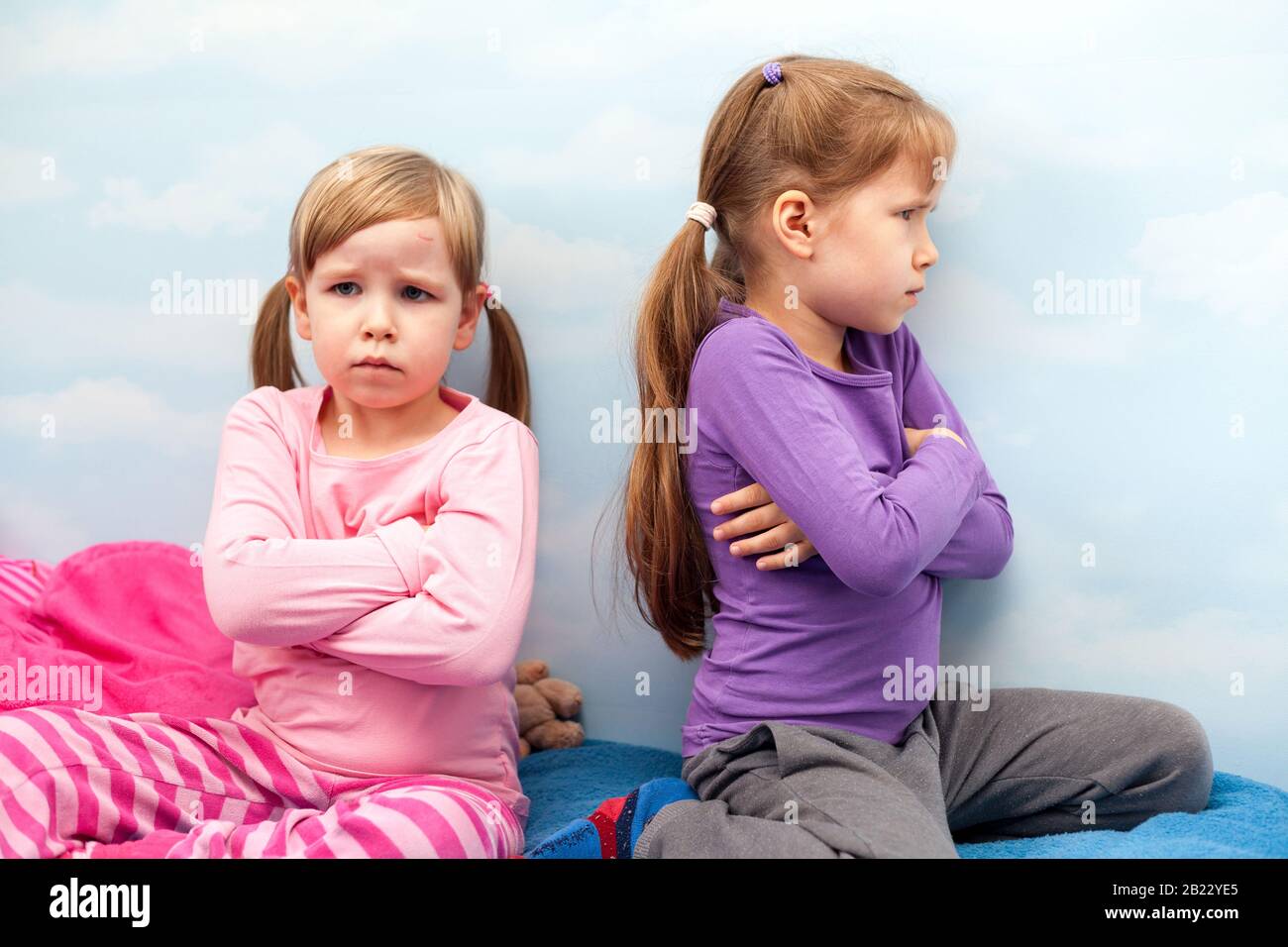 Two young little girls, sisters offended at each other, siblings conflict, fight, taking offence sitting back to back concept. Children, kids family Stock Photo