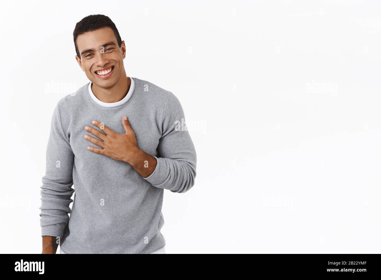 Happy and pleased, flattered hispanic man thanking for praises, holding hand on chest and smiling grateful, saying my pleasure, express gratitude and Stock Photo