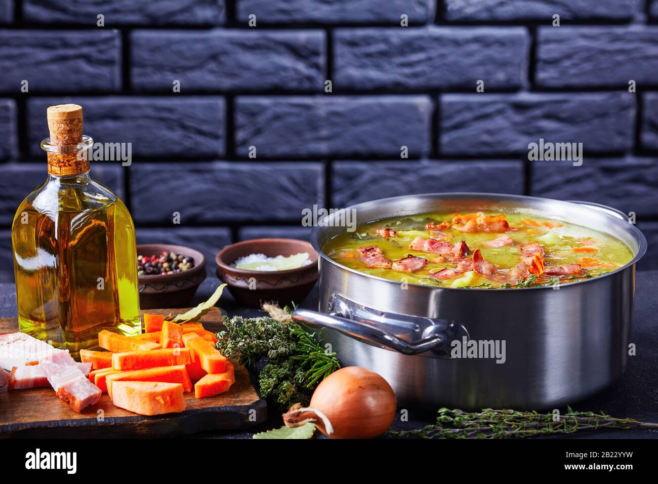 Authentic split pea soup with bacon, pork ham, carrot, potato with thyme served on a pot on dark concrete background with ingredients in front of the Stock Photo