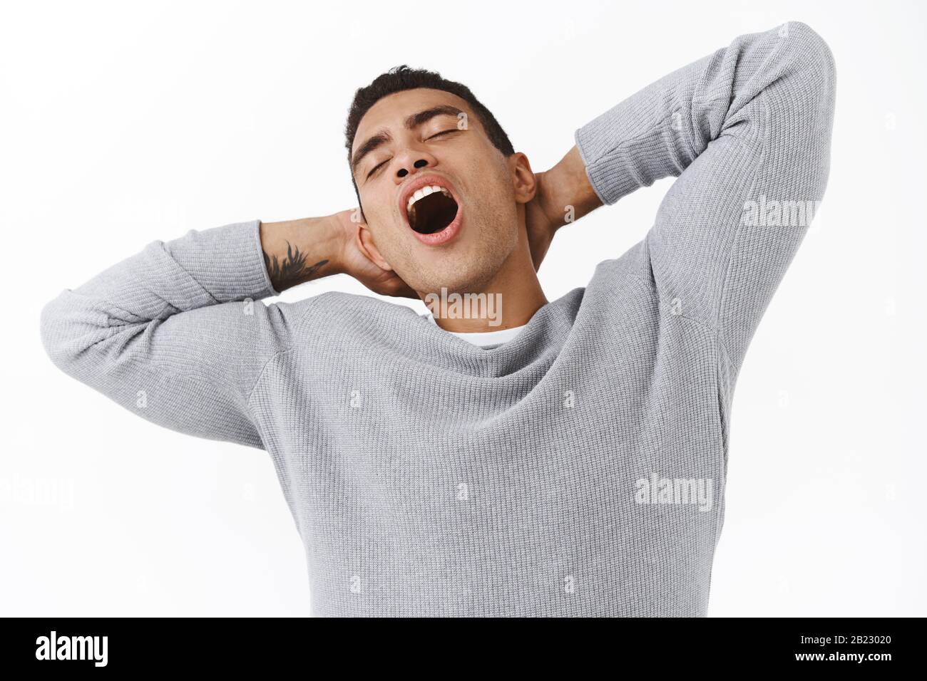 Close-up lazy handsome young hispanic guy with athletic body, stretching and holding hands behind head, yawning with closed eyes tired, feeling sleepy Stock Photo