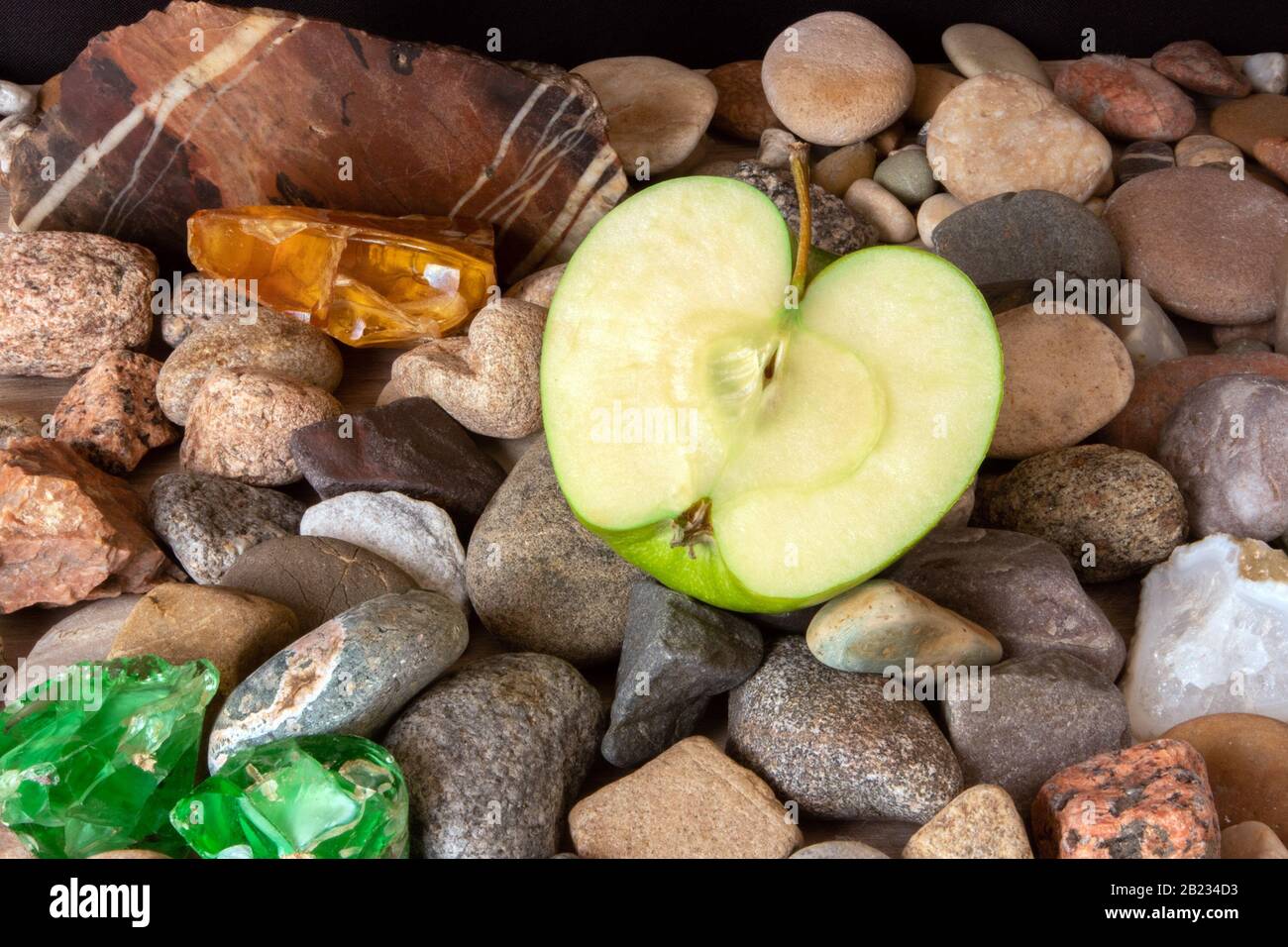 Half of big green apple with stem lying on pebble decorated with agate, jasper and colored glass Stock Photo