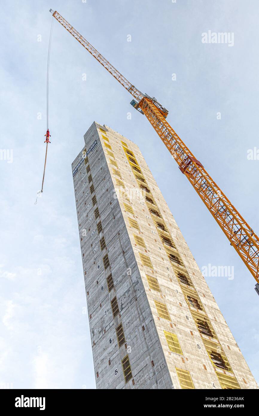Looking upwards at an 18 storey concrete construction lift shaft with a yellow tower crane framing the building Stock Photo