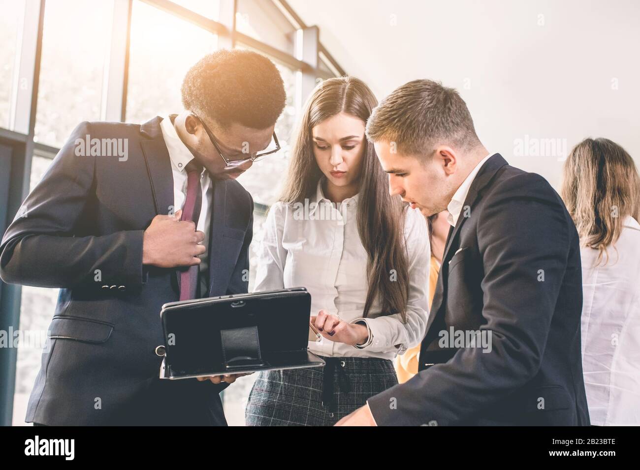Business people in office having conversation and using digital tablet. Cheerful young African American man and Caucasian man and woman having busines Stock Photo