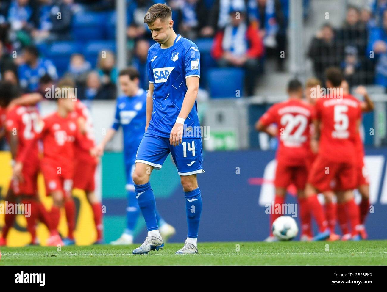 Sinsheim, Germany. 29th Feb, 2020. Football: Bundesliga, 24th matchday, 1899 Hoffenheim - Bayern Munich, PreZero Arena. Hoffenheim's Christoph Baumgartner crosses the square disappointed. In the background the players of FC Bayer Munich are cheering for the 0:3. Credit: Tom Weller/dpa - IMPORTANT NOTE: In accordance with the regulations of the DFL Deutsche Fußball Liga and the DFB Deutscher Fußball-Bund, it is prohibited to exploit or have exploited in the stadium and/or from the game taken photographs in the form of sequence images and/or video-like photo series./dpa/Alamy Live News Credit: d Stock Photo