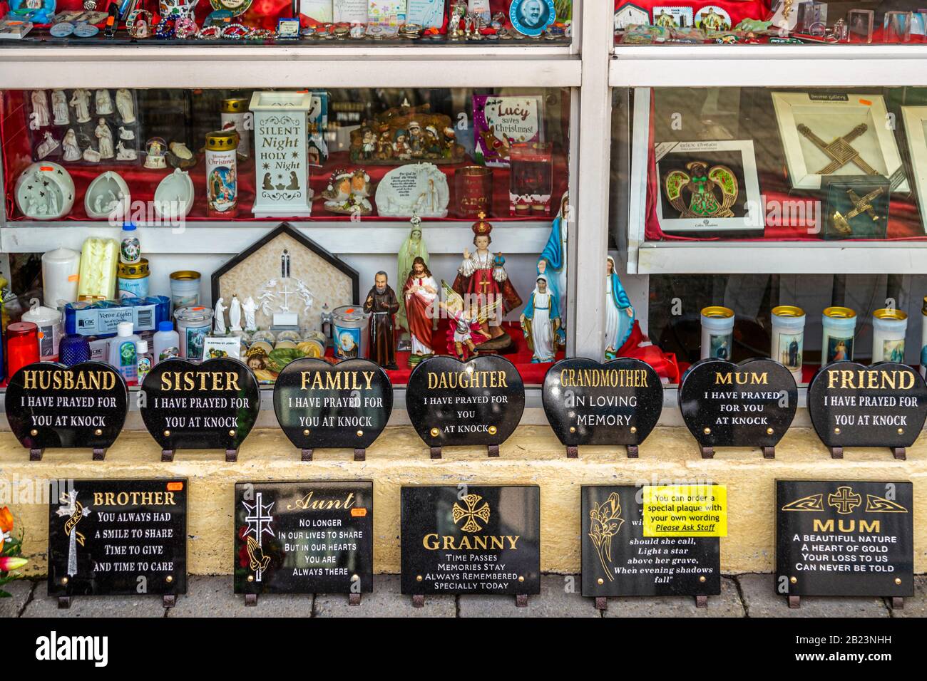 A shop window near the Knock Shrine Marian pilgrimage site in County Mayo, Ireland, displays memorial plaques reading "I have prayed for you at Knock" alongside religious statues, candles and other devotional souvenirs. Stock Photo