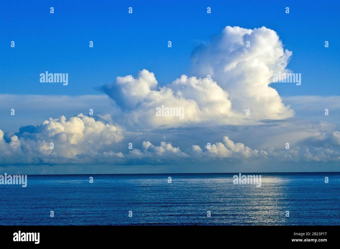 Cumulo Nimbus clouds on the horizon, lit from the side and reflected in the sea. Stock Photo