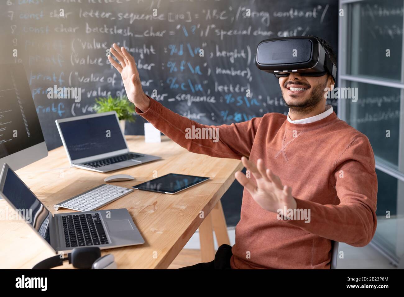 Happy young programmer wearing vr goggle sitting by desk with laptops ...